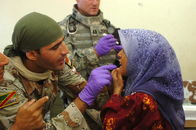 Iraqi Army Pvt. Ahmed Abdualsuda, a medic with the 2nd Brigade, 9th Iraqi Army Division (Mechanized) examines a little girl's mouth which is causing her pain at a school set up as a make-shift clinic during a combined medical effort near Bassam,...