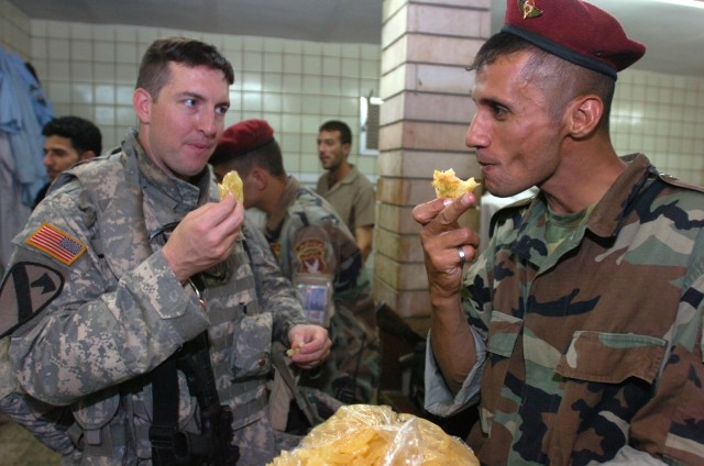 Portland, Ore., native, Capt. Jason Lewis, a Civil Affairs officer with the 2nd Brigade Combat Team, 1st Cavalry Division, shares a sweet snack with an Iraqi soldier during a visit to a hussainiyah, a Sunni place of worship, in the Karkh neighborhood...