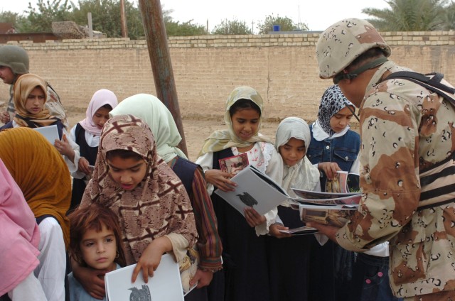 An Iraqi Army soldier from the 3rd Battalion, 2nd Brigade, 9th Iraqi Army Division (Mechanized) hands out comic books, crayons and other goodies to children at an elementary school in Jerf Al-Mila, Iraq Oct. 17 as part of the Iraqi Army's "Junior...