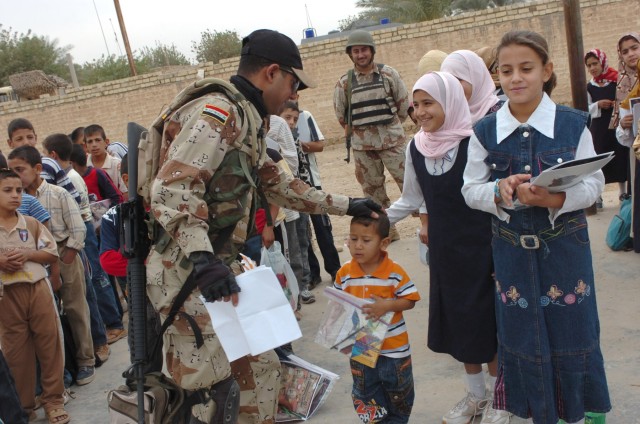 The Iraqi Army "junior hero," an Iraqi soldier from the 3rd Battalion, 2nd Brigade, 9th Iraqi Army Division (Mechanized) talks with children at an elementary school in Jerf Al-Mila, Iraq Oct. 17 during a "Junior Hero" event at the school. The...