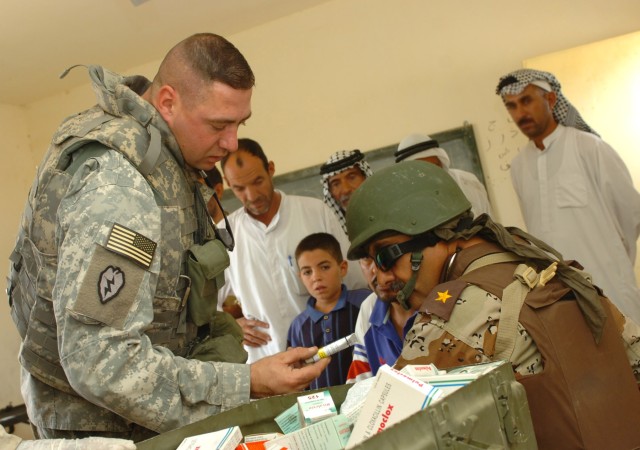 Staff Sgt. Paul Arenz (left), a medic for the 4th Battalion, 227th Aviation Regiment, 1st Air Cavalry Brigade, hands medication to an Iraqi doctor from the 3rd Brigade, 6th Iraqi Army Division who is treating an elderly Iraqi man for a skin condition...