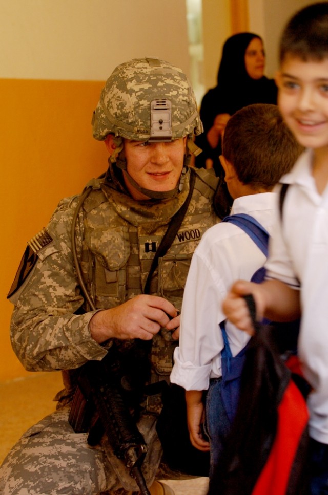 Blackwell, Okla., native Capt. Jesse Wood, project officer for Battery A, 3rd Battalion, 82nd Field Artillery Regiment, helps a student put his backpack on during the Al Hamza Elementary School re-opening in central Baghdad's Qadisiyah...