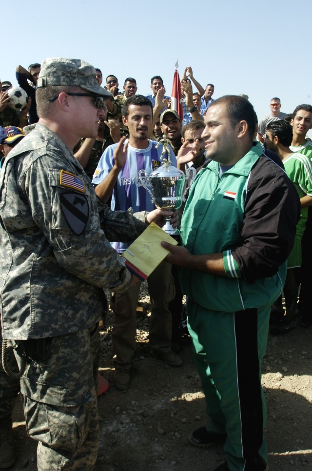 Huntsville, Ala., native, Lt. Col. Dale Kuehl, commander of the 1st Battalion, 5th Cavalry Regiment, presents the first-place trophy to Rafeid Khaleiel, the coach of the Forsan Al Rafadeen (FAR) soccer team at the end of a soccer tournament hosted by...