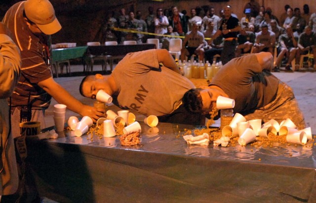 Two Soldiers with the 3rd Brigade Combat Team, 1st Cavalry Division, try desperately to pour cold peas into a water bottle without the use of their hands during the Fear Factor Baqouba competition at Wood Dining Facility, Forward Operating Base...