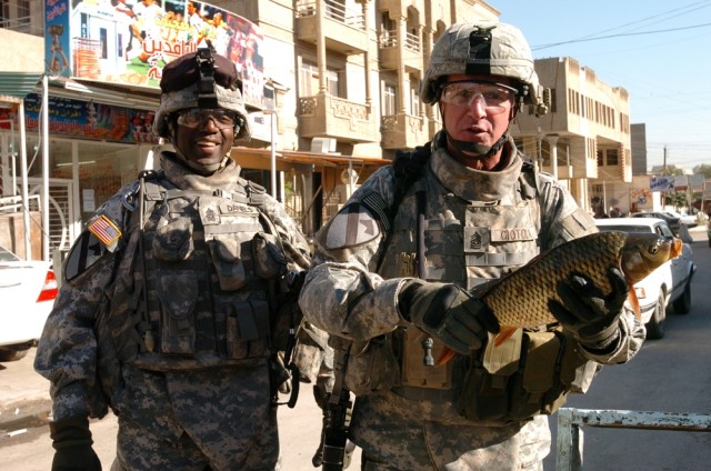 Command Sgt. Maj. Neil Ciotola (right), the senior noncommissioned officer for the Multi-National Corps - Iraq, holds up a fish during a walk-through of a market in western Baghdad along with Command Sgt. Maj. James Daniels, the top NCO with 4th Squa...