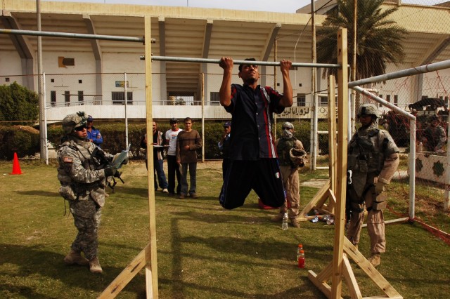 Sgt. Brian McCain, Headquarters and Headquarters Troop, 4th Squadron, 2nd Stryker Cavalry Regiment, attached to the 2nd Brigade Combat Team, 1st Cavalry Division, watches as a Karkh resident who hopes to join the Iraqi police force, performs pull-ups...