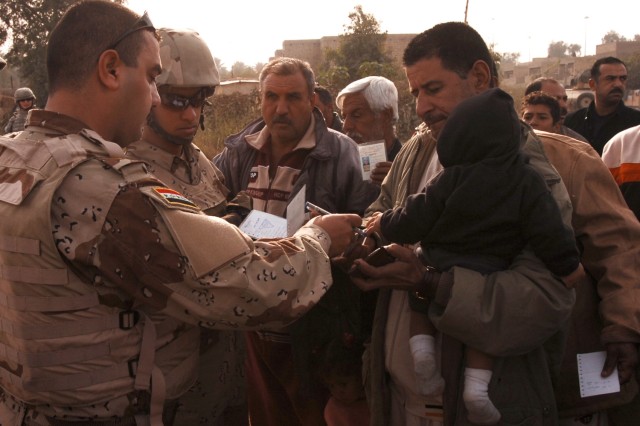 An Iraqi Army soldier checks the identification of a man before he enters the distribution site at the Quds Camp in central Baghdad's Janeen neighborhood during a kerosene heater and blanket distribution conducted by Soldiers from 3rd Battalion,...