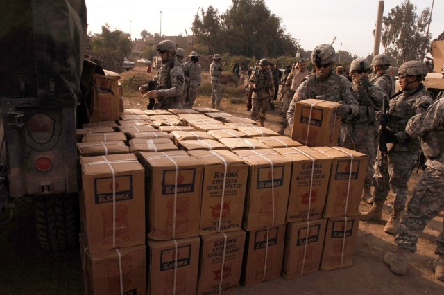 Spc. Gregory Clarke, 3rd Battalion, 82nd Field Artillery Regiment, 2nd Brigade Combat Team, 1st Cavalry Division, stacks boxes of kerosene heaters for distribution during a humanitarian aid mission at the Quds Camp in central Baghdad's Janeen...
