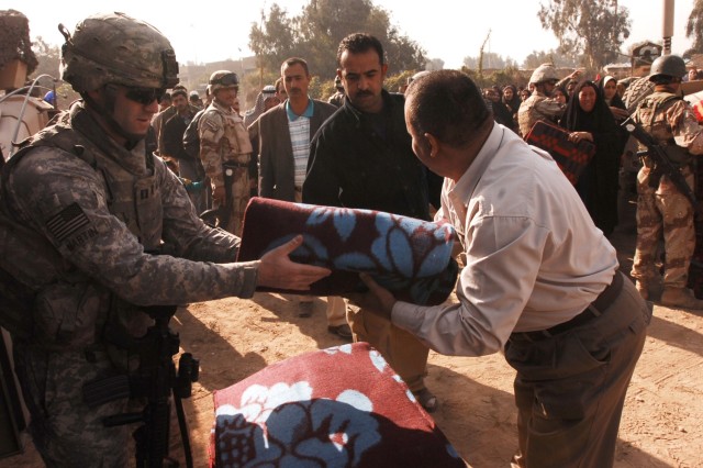 Capt. Todd Martin, Battery A, 3rd Battalion, 82nd Field Artillery Regiment, 2nd Brigade Combat Team, 1st Cavalry Division, hands a wool blanket to Janeen Neighborhood Advisory Council chairman Udai Ra'ed, for distribution to a resident of the Quds...