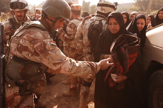 A resident of the Quds Camp in the central Baghdad Janeen neighborhood receives a wool blanket from an Iraqi Army soldier during a blanket and kerosene heater distribution mission conducted by Soldiers from 3rd Battalion, 82nd Field Artillery...