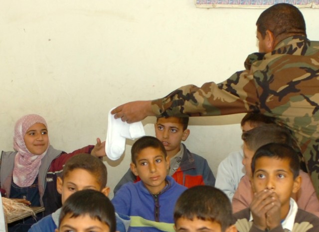 JERF AL MILA, Iraq --  An Iraqi Army solder from the 3rd Battalion, 2nd Brigade, 9th Iraqi Army Division (Mechanized) gives socks to an Iraqi girl at an elementary school in Jerf Al Mila, in northwest Baghdad, Dec. 17 during an event in which...