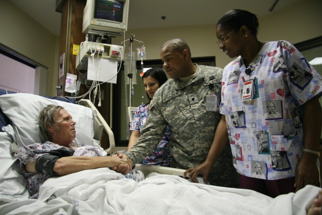 Spc. Warren Frazier shakes Navy veteran Calvin Cavaness&#039; hand during a bed-side visit flanked by colleagues Renee Araujo (left center) and Sheila Robinson-Bird