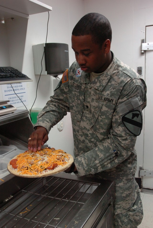 Human resources specialist Spc. Everett Stubbs with Headquarters Company, 1st Brigade Special Troops Battalion, 1st Brigade Combat Team, 1st Cavalry Division, puts the final touches on his pizza before putting it into the oven during a Soldier apprec...