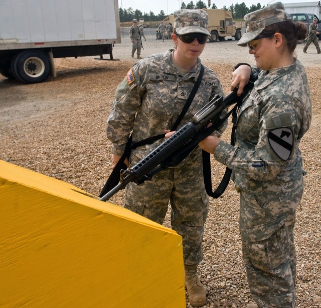 Pfc. Karen Medlin inspects fellow intelligence analyst Spc. Cassandra Perry's weapon at a clearing barrel before entering the Forward Operating Base Sword dining facility for lunch March 14. The clearing barrels at the Joint Readiness Training...