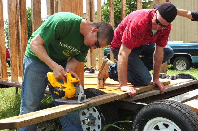 While building a mobile equipment trailer for the Habitat for Humanity organization, Pfc. Jason Boldt (right), an engineer with Company E, 2nd "Stallion" Battalion, 8th Cavalry Regiment, who hails from Southbend, Ind., holds a piece of wood still...