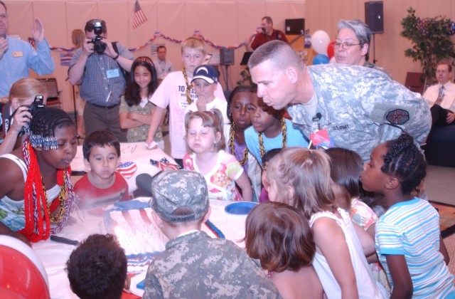 Fort Riley Garrison Commander helps children blow out candles, celebrating Army Birthday