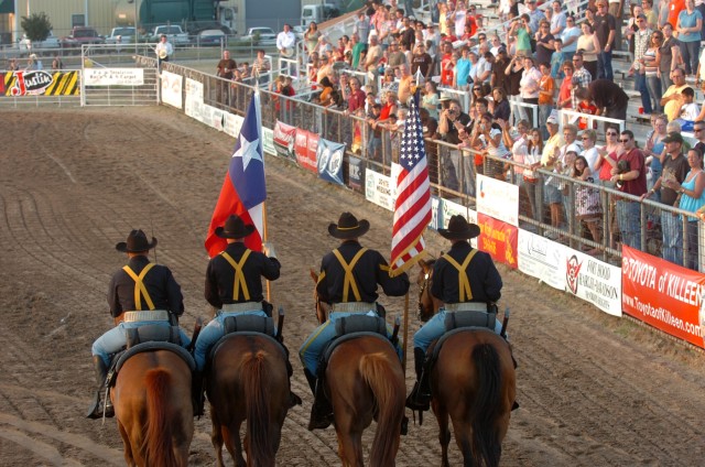 Prior to the start of a rodeo, a large crowd observes as a color guard made up of four mounted troopers from the 1st Cavalry Division's Horse Cavalry Detachment ride to the spot where they will post the national colors along with the Texas state flag...