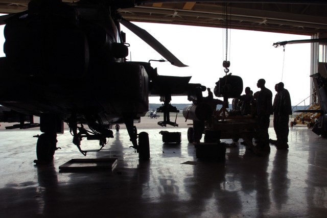 Crew chiefs from 1st "Attack" Battalion, 227th Aviation Regiment, 1st Air Cavalry Brigade, 1st Cavalry Division, silhouetted by the harsh light of the sun, work on a hoisted AH-64D Apache attack helicopter engine during their daily maintenance...
