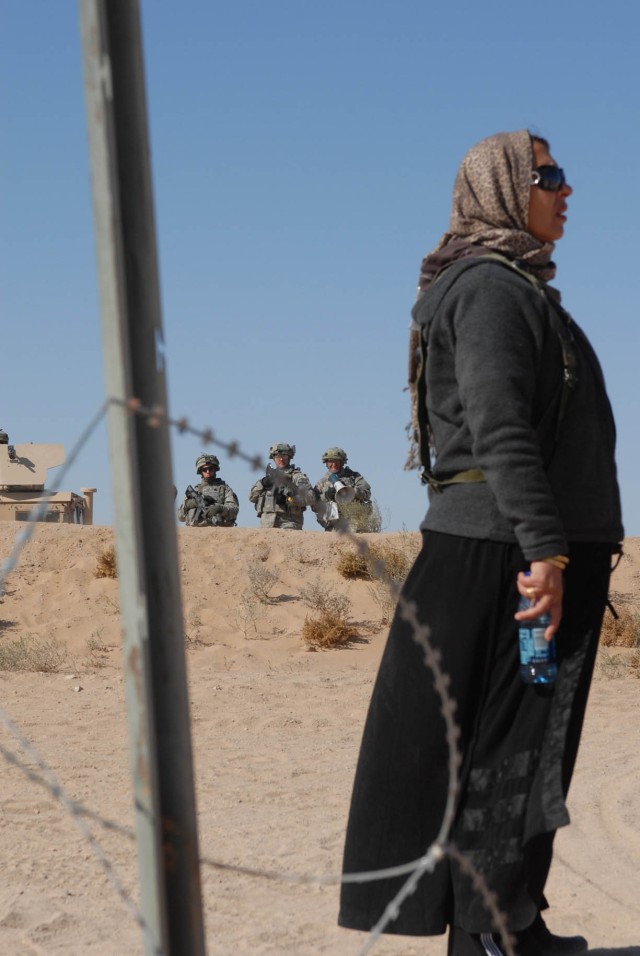 An actress portraying an Iraqi civilian stands and listens to instructions given by a unit translator over a loud speaker upon her gaining entrance to the unit's controlled entry point outside of their forward operating base located at the...