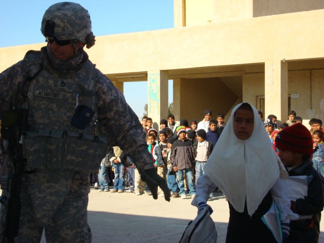 Sgt. 1st Class Kevin Albrecht, the 4th STB, 4th BCT, 1st Cav. Div. personnel security detachment platoon sergeant, reaches for a school bag after handing a different bag to an Iraqi girl at the Ur Primary School, located in the southern Iraqi city...