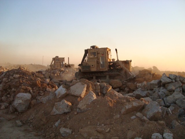 BAGHDAD - Two 25-ton bulldozer operators push massive piles of debris off the side of the road in northern Baghdad during a joint route sanitation mission conducted by the 46th Engineer Combat Battalion (Heavy) and 6th Iraqi Army engineers.  The...