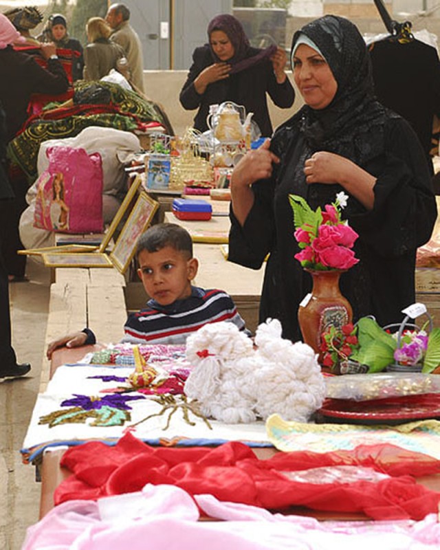 BAGHDAD- A local Iraqi woman from the Mahmudiyah Qada stands by her table of merchandise with her son during the Women's Bazaar hosted by Task Force 1st Combined Arms Battalion, 63rd Armor Regiment at FOB Mahmudiyah, Feb 17. Homemade products and Ira...