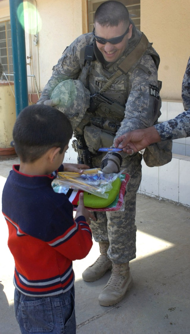 BAGHDAD - Capt. Marcus Long, a native of Patton, Mo., assigned to the National Police Transition Team, currently attached to the 3rd BCT, 82nd Airborne Division, gives an Iraqi child an assortment of school supplies during a distribution event Feb. 2...