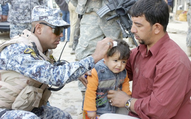 BAGHDAD - Iraqi Sgt. Maj. Thamir (left), assigned to the 1st National Police Brigade, 1st NP Div., provides first aid to a little boy in the central Baghdad neighborhood of Karada. A combined Iraqi and Multi-National Division-Baghdad patrol was on th...