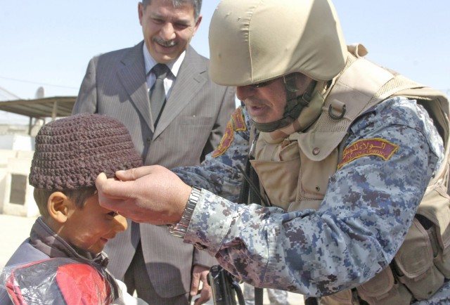 Baghdad - Col. Taria, operations chief, 1st National Police Brigade, 1st NP Division, places a hat on an Iraqi boy as Mr. Salam Hanoon, a district councilman from the Karada neighborhood, looks on during a school supply distribution event at the Qair...