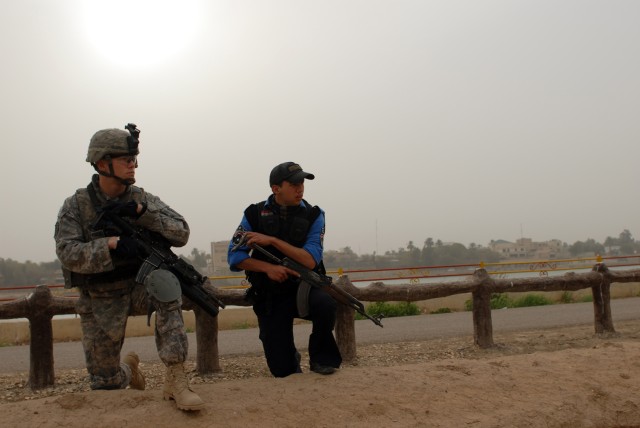 BAGHDAD - Spc. Zachery Hughes, a team leader assigned to Troop B, 5th Squadron, 73rd Cavalry Regiment, 3rd Brigade Combat Team, 82nd Airborne Division, is mirrored by Ali Falaha, an Iraqi policeman, while kneeling in Abu Nawas Park on the banks of...