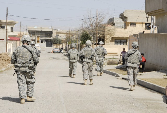 Several Soldiers with Battery B, 2nd Battalion, 82nd Field Artillery Regiment., 3rd Heavy Brigade Combat Team, 1st Cavalry Division, walk along an urban street in 7 Nissan, a neighborhood in northern Mosul. This and other streets like it in the area ...