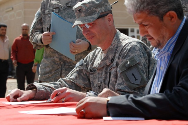 BAGHDAD – Col. Joseph Martin (left), commander, 2nd Brigade Combat Team, 1st Infantry Division, signs the transfer documentation that officially hands over four Coalition funded public works sub-stations to the Government of Iraq with the deputy mayo...