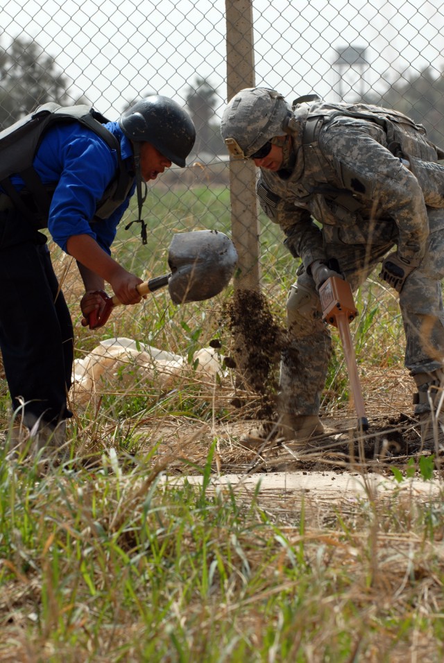 Sgt. Michael Tornincasa (right), from Struthers, Ohio, assigned to the 2nd Battalion 'Strykers,' 112th Infantry Regiment, 2nd Brigade Combat Team, 1st Infantry Division, yells words of encouragement to an Iraqi policeman while digging a hole where th...