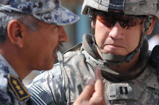 BAGHDAD - An National Policeman speaks with Capt. Carlos Ortiz (right) of Battery A, 1st Battalion, 319th  Airborne Field Artillery Regiment during a Coalition forces inspection of an Iraqi Security Forces checkpoint March 20 in the Al Karradah...