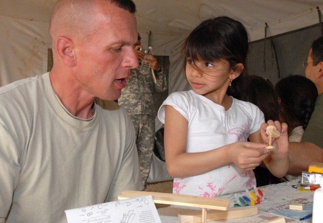 CAMP VICTORY, Iraq - Five-year-old Mariem looks at Maj. Gary Farley, a MiTT team advisor for the Iraqi Ground Forces Command, Multi-National Corps -Iraq, who hails from Gowanda, N.Y., for assurance as she assembles the wheelbase for a model plane Mar...