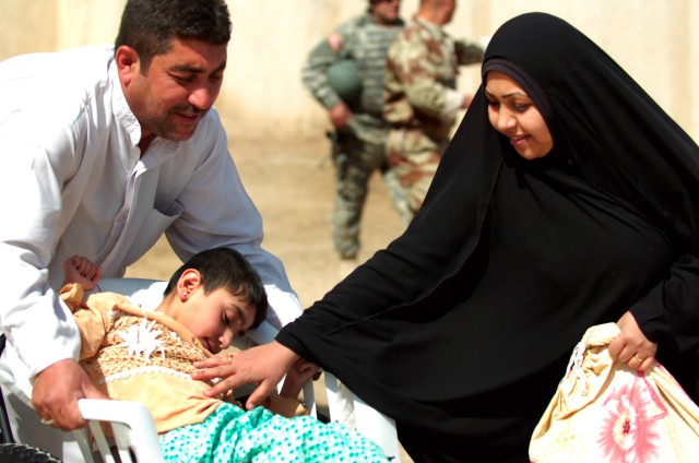 BAGHDAD-An Iraqi couple braces their child in his new wheelchair as they lower him off a sidewalk.   The wheelchair, provided by the 11th Iraqi Army Division, was part of a humanitarian aid mission at the New Iraq School in the Adhamiyah district...