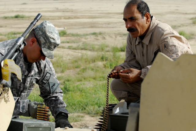 Staff Sgt. Joseph Romano (left), an instructor with the Multi-National Security Transition Command-Iraq (MNSTC-I), and an Iraqi Armor School student load rounds for an M1A1 Abrams 240C machine gun in preparation for Iraqi Soldiers to receive training...