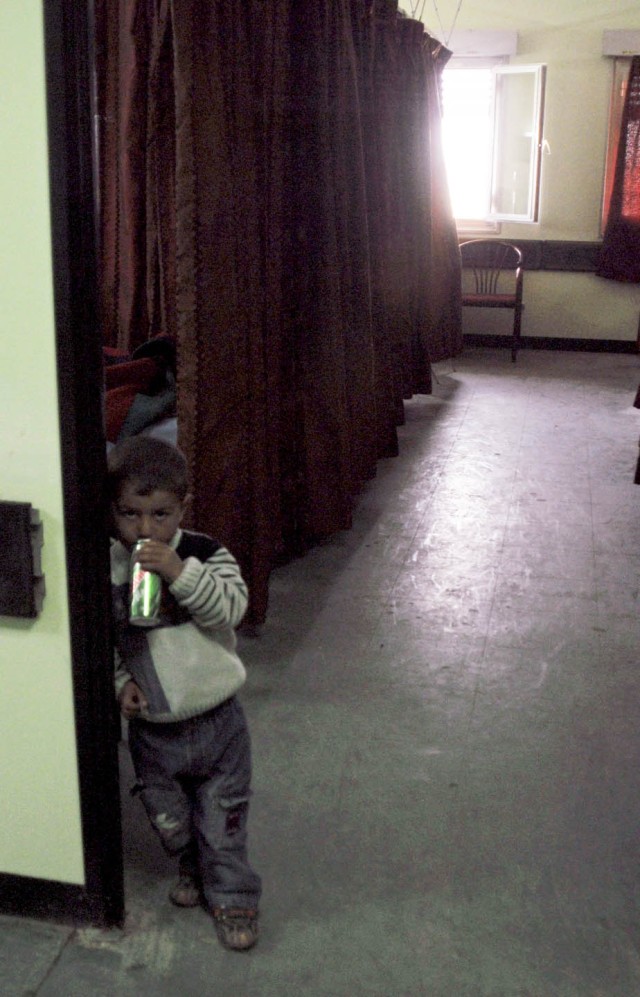 A little boy stands in the doorway of a relative's hospital room, lit by sunlight through a window on the room's far wall. The windows of the Alsalam Hospital in Mosul, Iraq were damaged in improvised explosive device concussions and are being replac...