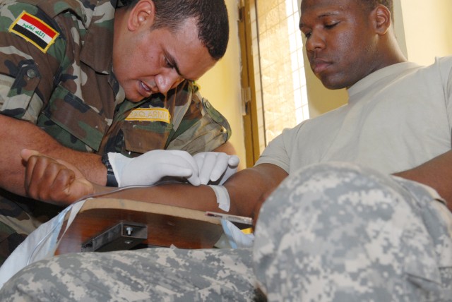 BAGHDAD - Sgt. 1st Class Gary Petty (right), division surgeon advisor with the 6th Iraqi Army Division Military Transition Team, demonstrates his trust in Iraqi medics March 25, by allowing Sgt. Maj. Shakir Kenyab Moktaf Farham, a medic with 6th IA D...