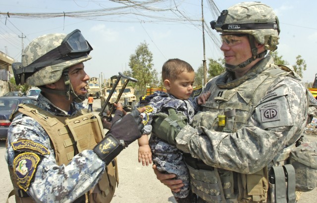 BAGHDAD -Capt. Clay White, of Williamsburg, Va., commander of Company C, 2nd Battalion, 505th Parachute Infantry Regiment, 3rd Brigade Combat Team, 82nd Airborne Division, talks to a National Police officer as he carries an Iraqi child wearing a...