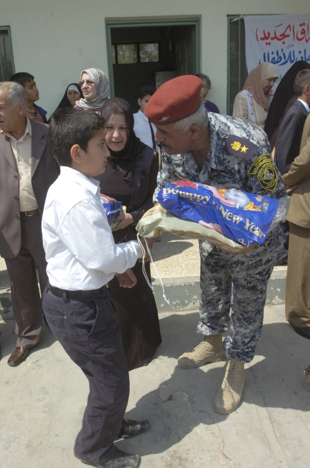 BAGHDAD - An National Police officer hands an Iraqi boy a bag of clothes and school supplies during a distribution event in the area of Sumer al-Ghadier April 1 in the 9 Nissan district of eastern Baghdad. District and NP officials invited...