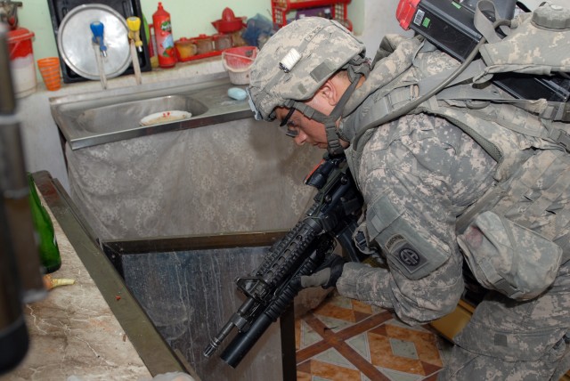 BAGHDAD - Downey, Calif. native, Spc. Martin Aguilar (right), a cannon crewmember assigned to Battery B, 1st Battalion, 319th Airborne Field Artillery Regiment, watches over the shoulder of an Iraqi National Policeman as they prepare to enter a...