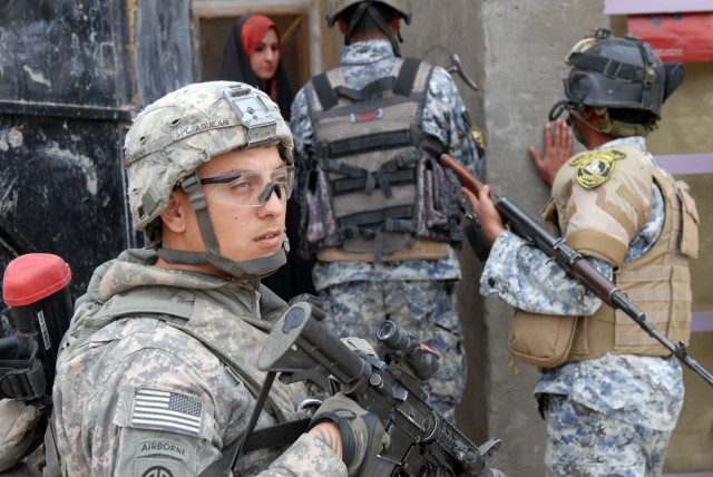 BAGHDAD - Spc. Martin Aguilar (left), a cannon crewmember from Downey, Calif., assigned to Battery B, 1st Battalion, 319th Airborne Field Artillery Regiment, gets ready to enter a house here March 30, with his Iraqi National Police partners during...