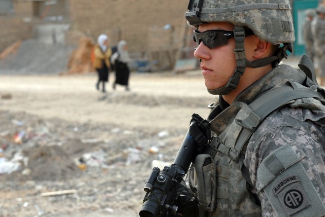 BAGHDAD - Pfc. Steven Cooper, a cannon crewmember and native of Boston, assigned to Battery B, 1st Battalion, 319th Airborne Field Artillery Regiment, 3rd Brigade Combat Team, 82nd Airborne Division, protects a cordon as Iraqi children walk to...