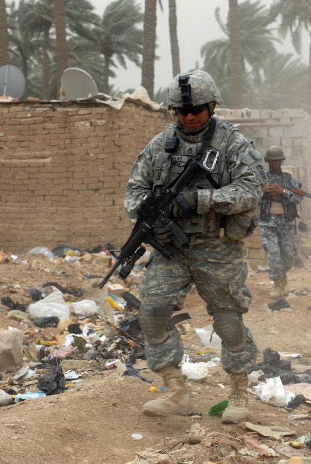 BAGHDAD - Staff Sgt. Roberto Moreno, a cannon crewmember, assigned to Battery B, 1st Battalion, 319th Airborne Field Artillery Regiment, leads an Iraqi National Policeman through a trash-lined alley during a joint operation. The operation was NP...