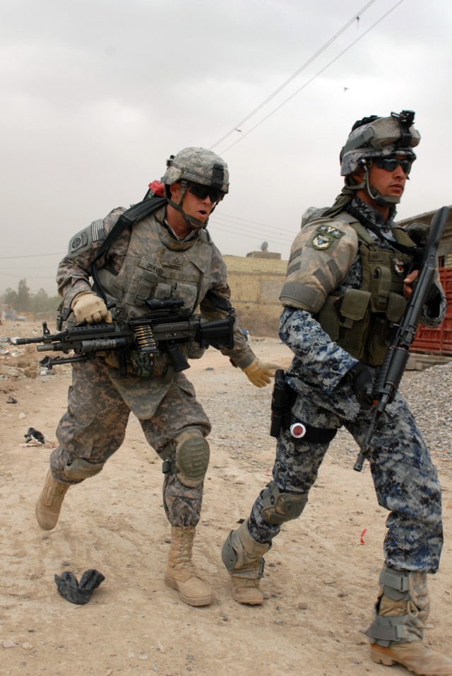 BAGHDAD - Pfc. Justin Graves, a cannon crewmember assigned to Battery B, 1st Battalion, 319th Airborne Field Artillery Regiment yells and gives encouragement to his Iraqi National Police partner during a joint operation. The operation was NP led...