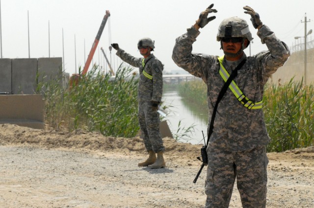 VICTORY BASE COMPLEX, Iraq -  Staff Sgt. David Arispe, of the 277th Engineer Company, attached to the 46th Engineer Battalion, 225th Engineer Brigade, from San Antonio, ground guides heavy equipment machinery using hand and arm signals while San...