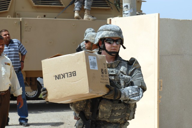BAGHDAD - Sgt. Kasandra Deutsch, a native of Pineville, La., who is a computer technician for the 225th Engineer Brigade, assists other Soldiers with unloading a 5-Ton truck of supplies that will be given to students of the Michal al-Hurria School...
