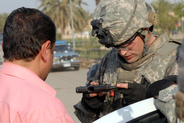 BAGHDAD - An Iraqi man watches on as Cpl. Cameron McNeel, an infantry team leader from Houston assigned to 1st Battalion, 5th Cavalry Regiment,  checks the serial number on the man's handgun with the serial number on the man's weapon's...
