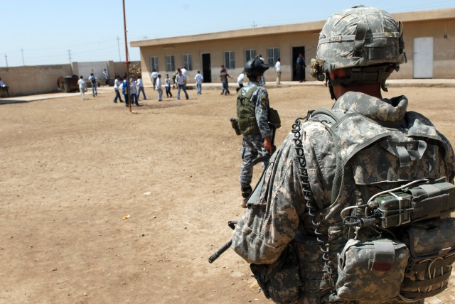 BAGHDAD - Staff Sgt. Tim Winn, a section sergeant cavalry scout from Anadarko, Okla., assigned to 1st Squadron, 7th Cavalry Regiment, 1st Brigade Combat Team, 1st Cav. Division, stands guard with an Iraqi National policeman at Akdha High School...